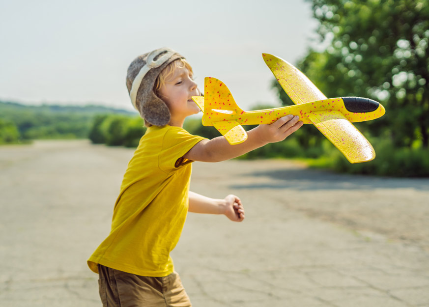 Kind spielt mit einem gelben Spielzeugflugzeug im Freien.