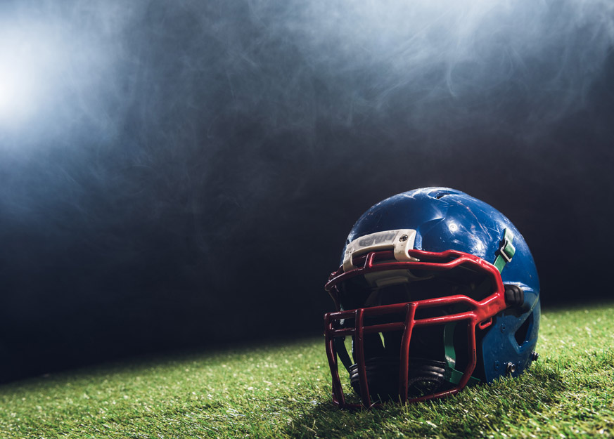 Blauer Football-Helm liegt auf Kunstrasen unter Stadionlicht.