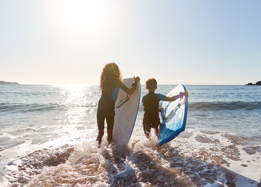 Zwei Kinder laufen am Strand mit Bodyboards ins Meer.